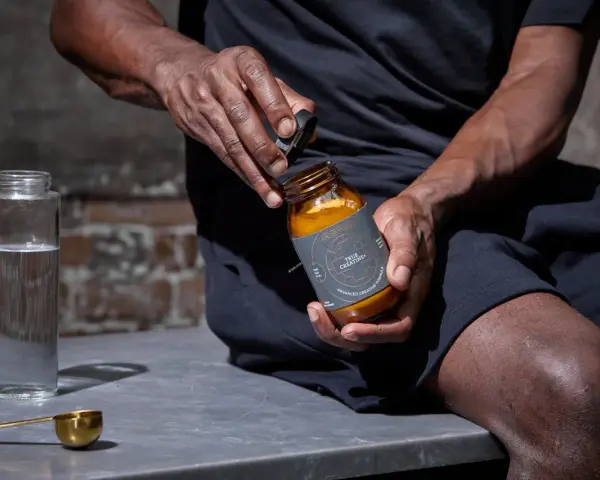 Hombre abre frasco de creatina. ¿La creatina te pone nervioso? Prepárate para tu ritual diario.