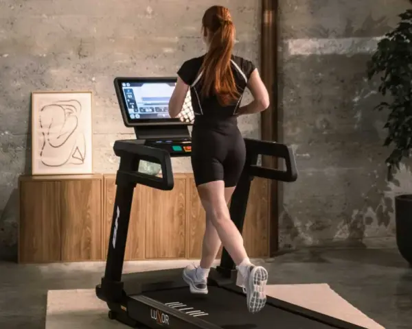 Mujer pelirroja corre en cinta, entrenando en casa con estilo.