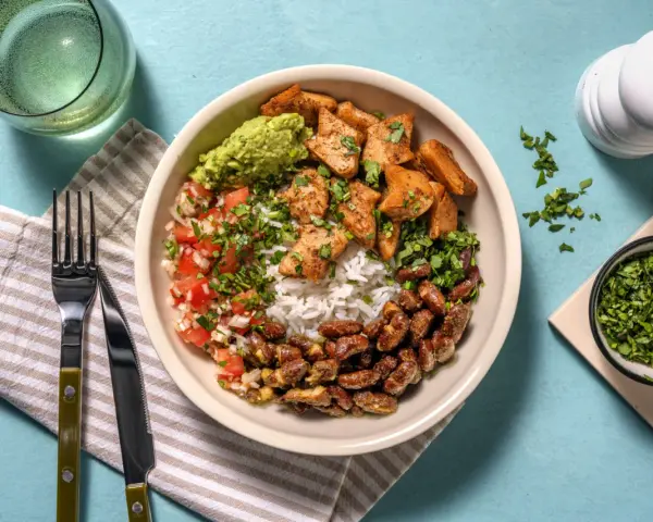 Bowl con arroz, frijoles, guacamole, pico de gallo y trozos de boniato y tofu, un festín de comidas vegetarianas ricas en proteínas.