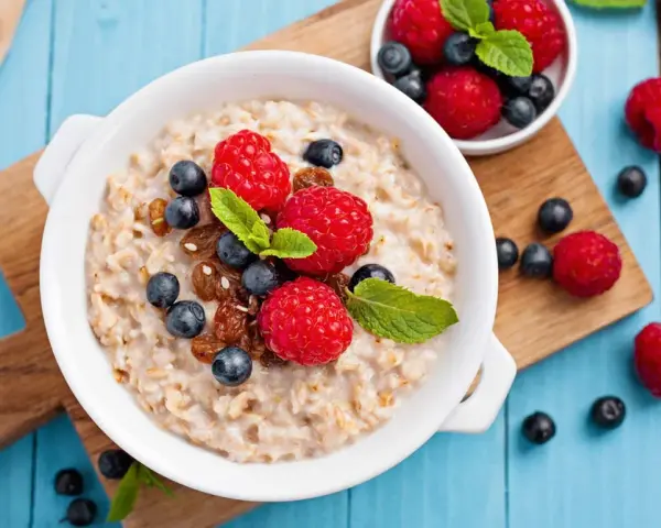 Un tazón de avena con frambuesas, arándanos y pasas. Descubre los beneficios de la avena por la noche para un descanso reparador.