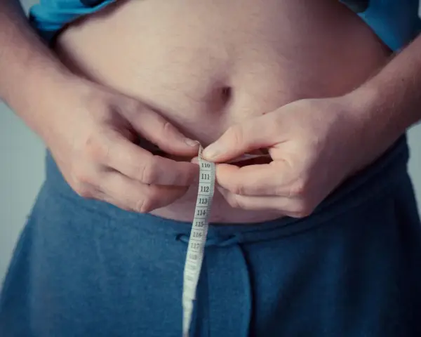 Man measuring waist with tape. A step towards understanding como activar la autofagia for better health.