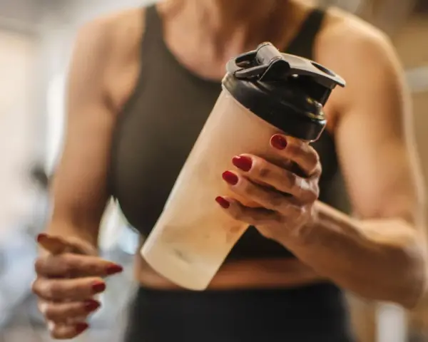 Mujer con uñas rojas sostiene un batido. ¿Los BCAA engordan? La respuesta depende de tu dieta.