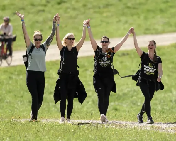 Cuatro mujeres celebran tomadas de la mano, con los brazos en alto, mientras caminan por un sendero. Su **velocidad media andando** parece alegre y enérgica.