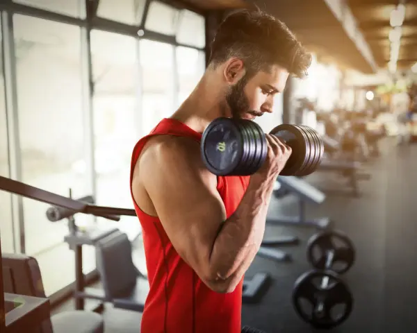 Hombre con barba entrenando bíceps con mancuerna en gimnasio. ¿Cuál es la mejor hora para entrenar?