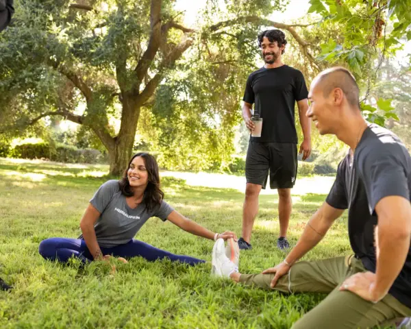 Un grupo de amigos hace estiramientos en un parque. Uno de ellos, que bebe un batido, bromea diciendo que "la creatina engorda", pero todos se ríen y siguen entrenando.
