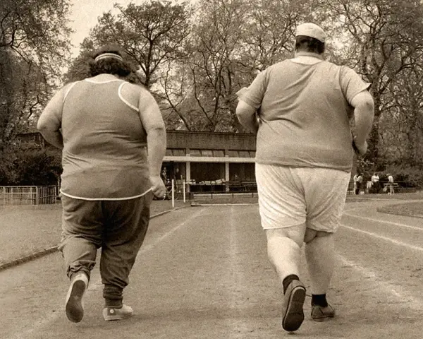 Dos personas con sobrepeso corren en una pista de atletismo. El andar adelgaza, y ellos lo saben.