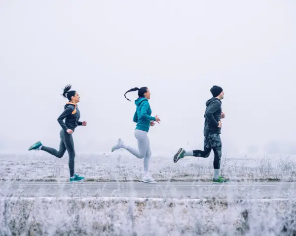 Tres personas corren en un paisaje nevado con ropa para correr en invierno.