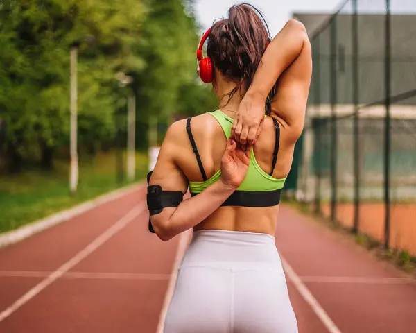 Mujer con cuerpo tonificado estirando el brazo sobre la cabeza en una pista de atletismo.