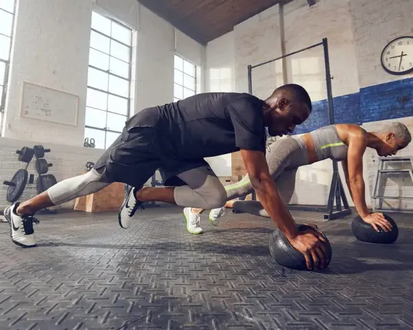 Pareja haciendo cardio en casa, en posición de plancha con balones medicinales.