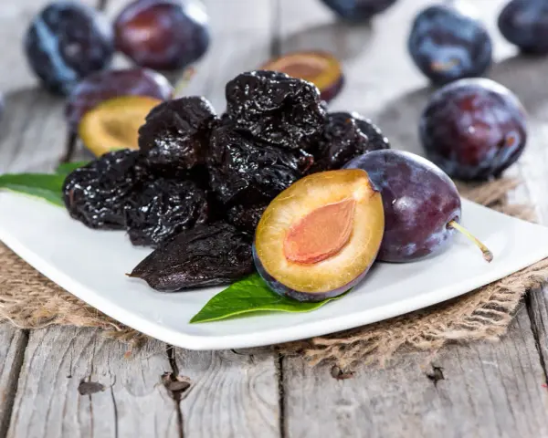Ciruelas pasas y ciruelas frescas en un plato blanco, perfectas para comer ciruelas pasas por la noche.