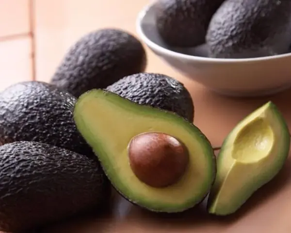 Aguacates frescos, uno cortado por la mitad mostrando su semilla, perfectos para comer aguacate todos los días y disfrutar de su cremosidad.