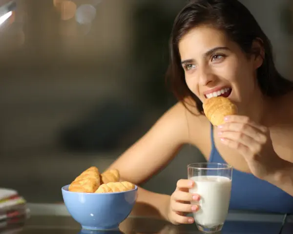 Mujer sonríe mientras come un croissant, pensando en qué picar entre horas que no engorde.
