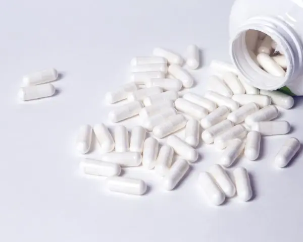 Cápsulas blancas derramadas de un frasco. Descubre para qué sirven los BCAA en mujeres y cómo pueden apoyar tu bienestar.