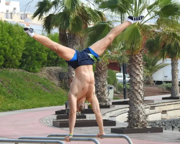 Hombre realizando ejercicios con tu propio peso, un pino en barras paralelas con palmeras de fondo.