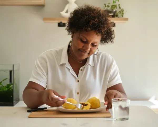 Mujer sonriente disfruta de croquetas de patata, un carbohidrato delicioso, con un vaso de agua.