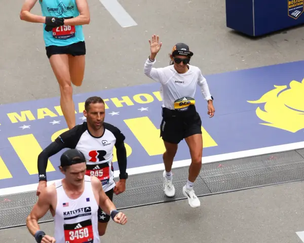 Corredores cruzan la meta en la media maratón de Europa. Una mujer saluda, celebrando su logro.