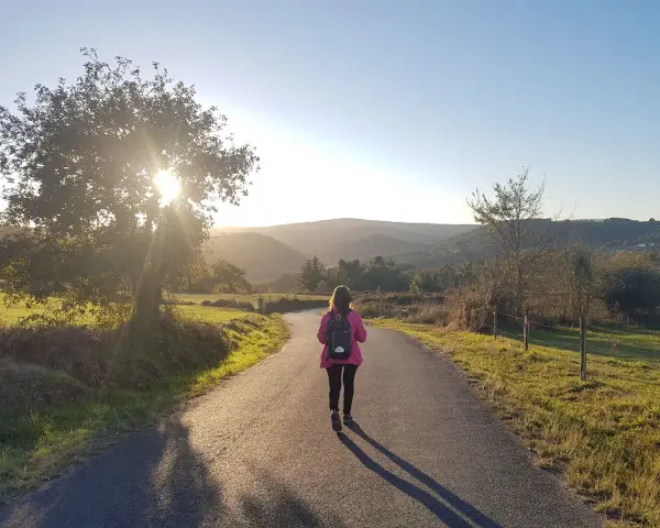 Una peregrina con mochila rosa camina por un sendero rural al atardecer, disfrutando del **camino de Santiago corriendo**.