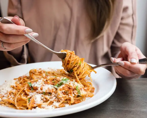 Mujer disfrutando un plato de pasta integral con salsa boloñesa y queso rallado. ¡Cuidado, la pasta integral engorda si no se consume con moderación!