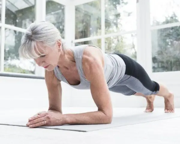 Mujer mayor haciendo plancha en su sala, demostrando que el fitness en casa es para todas las edades.
