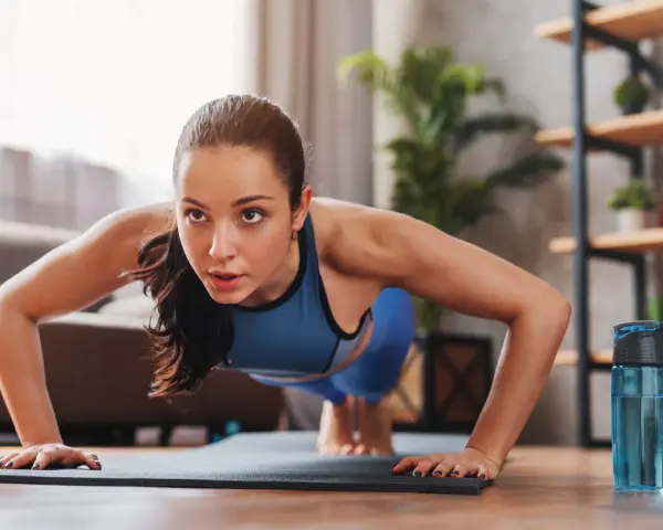 Mujer concentrada haciendo flexiones, parte de sus ejercicios de fuerza en casa.