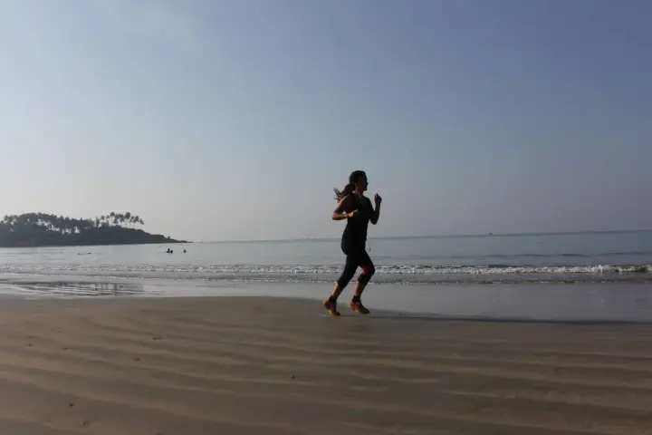 Mujer corriendo en la playa al amanecer, con el mar y una isla con palmeras al fondo.