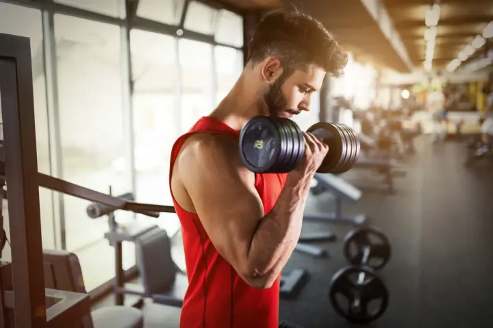 Hombre con barba entrenando bíceps con mancuerna en gimnasio. ¿Cuál es la mejor hora para entrenar?