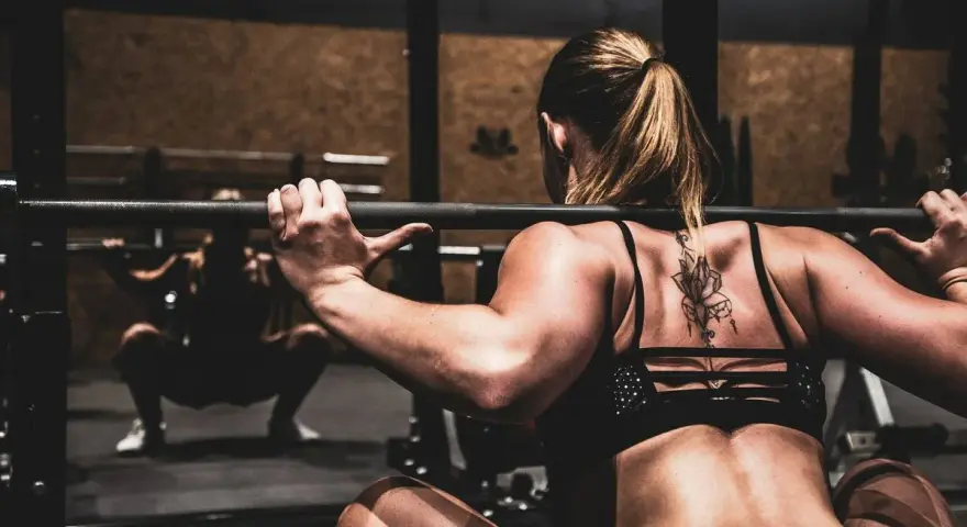 Mujer haciendo sentadillas con barra, un ejercicio clave para saber como ganar masa muscular rápido.