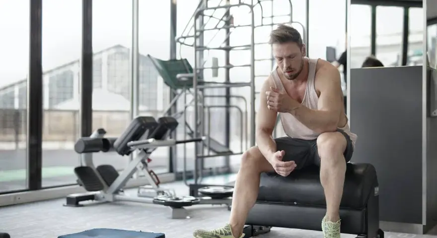 Hombre sentado en un banco de gimnasio, reflexionando sobre cuanto descansar entre series.