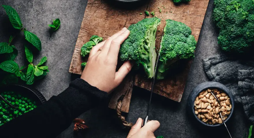 Manos cortando brócoli, un alimento rico en silicio, junto a guisantes y cacahuetes.
