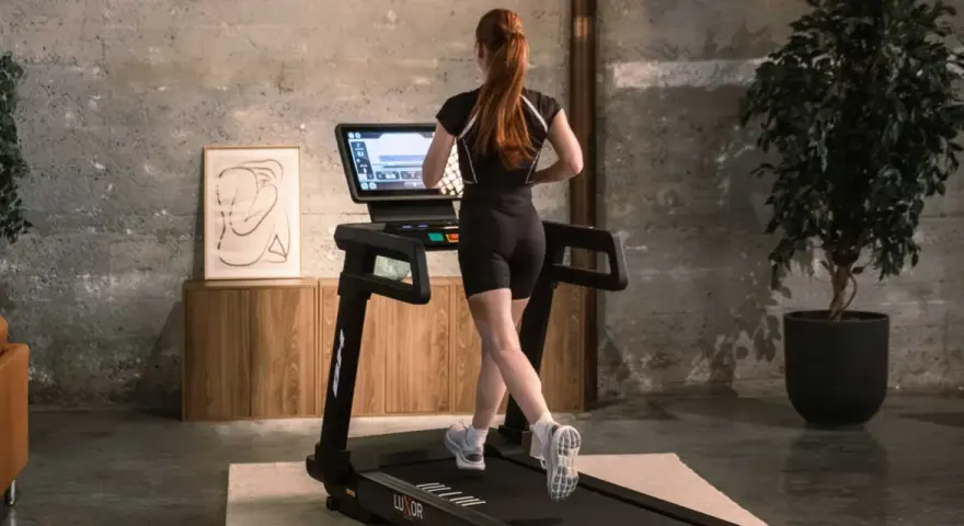 Mujer pelirroja corre en cinta, entrenando en casa con estilo.