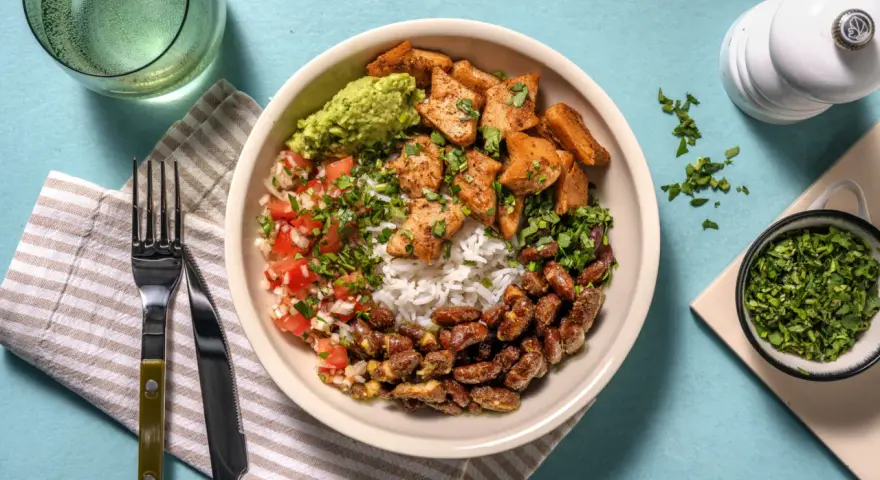 Bowl con arroz, frijoles, guacamole, pico de gallo y trozos de boniato y tofu, un festín de comidas vegetarianas ricas en proteínas.