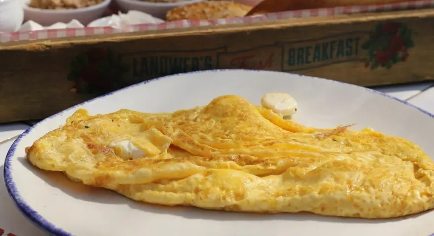 Tortilla francesa dorada en plato blanco, con un toque de queso. ¡Cuidado, la tortilla francesa engorda si no la acompañas con ensalada!
