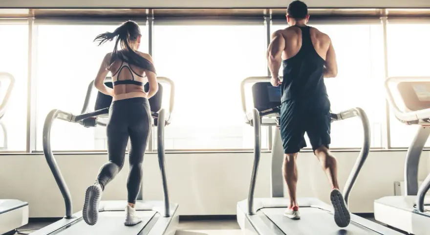 Hombre y mujer corriendo en cintas de correr, disfrutando de su rutina de cardio en ayunas.