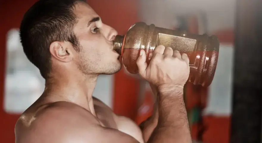 Hombre bebiendo de una botella grande, preparándose para el entrenamiento. ¿Cuántos gramos de pre entreno tomar?