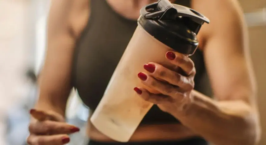 Mujer con uñas rojas sostiene un batido. ¿Los BCAA engordan? La respuesta depende de tu dieta.