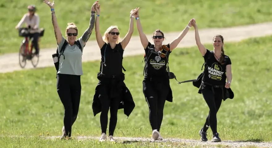 Cuatro mujeres celebran tomadas de la mano, con los brazos en alto, mientras caminan por un sendero. Su **velocidad media andando** parece alegre y enérgica.