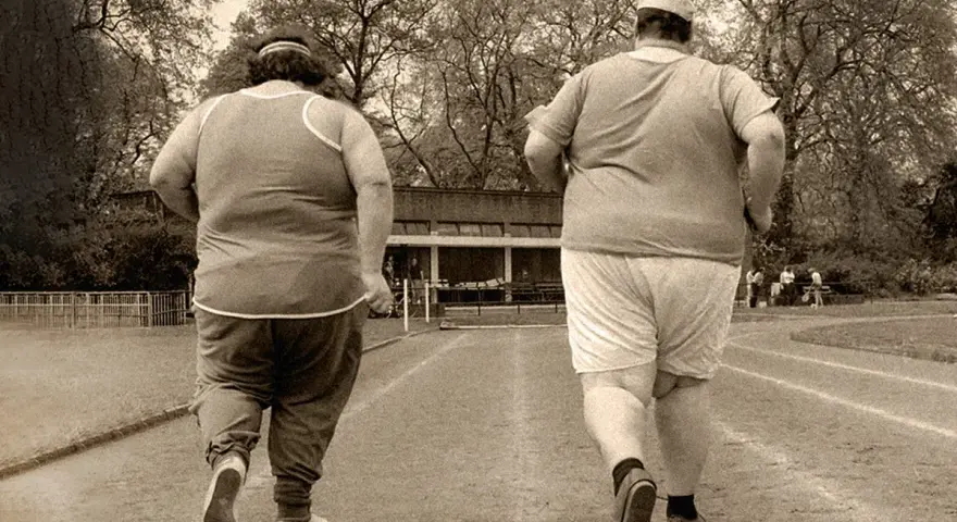 Dos personas con sobrepeso corren en una pista de atletismo. El andar adelgaza, y ellos lo saben.