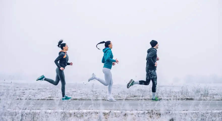 Tres personas corren en un paisaje nevado con ropa para correr en invierno.