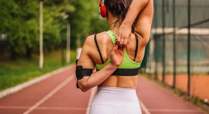 Mujer con cuerpo tonificado estirando el brazo sobre la cabeza en una pista de atletismo.