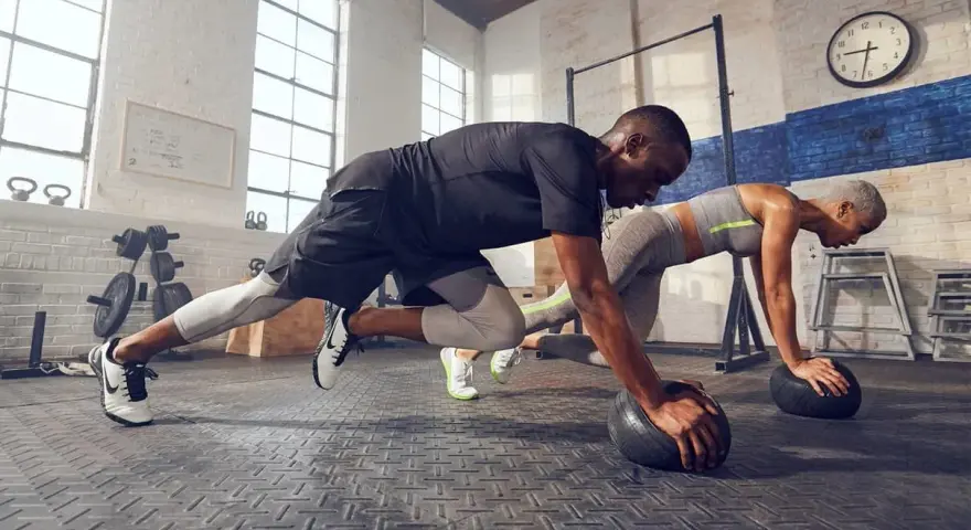 Pareja haciendo cardio en casa, en posición de plancha con balones medicinales.