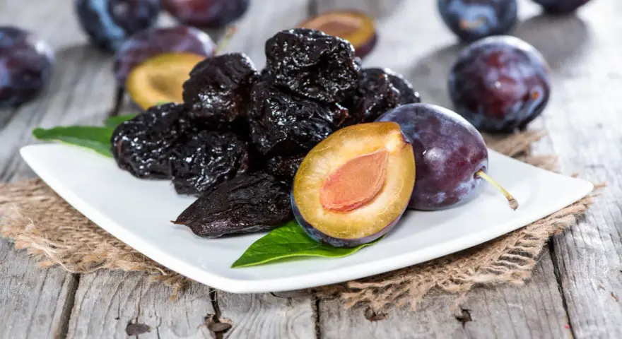 Ciruelas pasas y ciruelas frescas en un plato blanco, perfectas para comer ciruelas pasas por la noche.