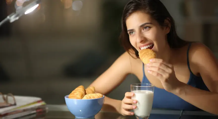 Mujer sonríe mientras come un croissant, pensando en qué picar entre horas que no engorde.