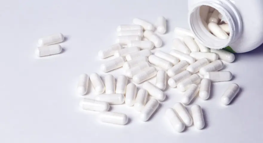 Cápsulas blancas derramadas de un frasco. Descubre para qué sirven los BCAA en mujeres y cómo pueden apoyar tu bienestar.