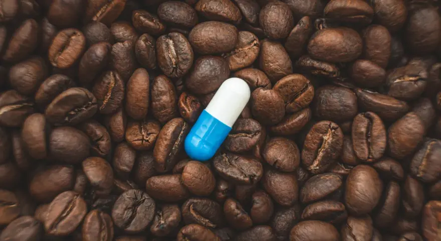 Una pastilla de cafeína azul y blanca descansa sobre granos de café tostados. ¿Cuánto tarda en hacer efecto una pastilla de cafeína?