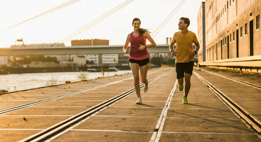 Pareja corriendo al atardecer, demostrando su **endurance crossfit**. El sol dorado ilumina su camino junto al río.