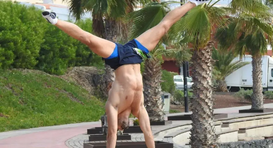 Hombre realizando ejercicios con tu propio peso, un pino en barras paralelas con palmeras de fondo.