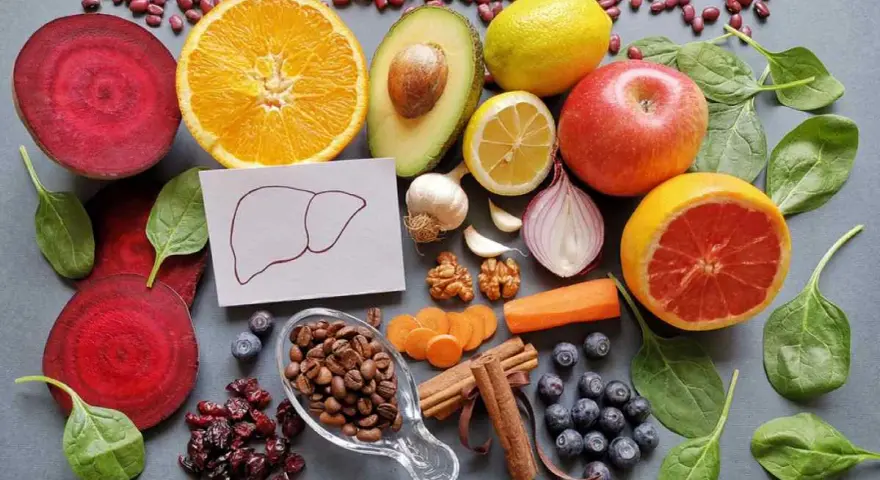 Una variedad de alimentos buenos para el hígado: remolacha, naranja, aguacate, limón, manzana, pomelo, espinacas, arándanos, café, canela, zanahoria, ajo, cebolla y nueces.