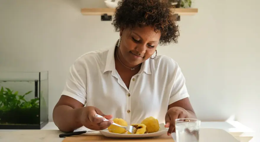 Mujer sonriente disfruta de croquetas de patata, un carbohidrato delicioso, con un vaso de agua.