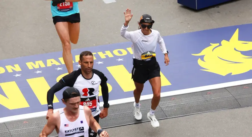 Corredores cruzan la meta en la media maratón de Europa. Una mujer saluda, celebrando su logro.
