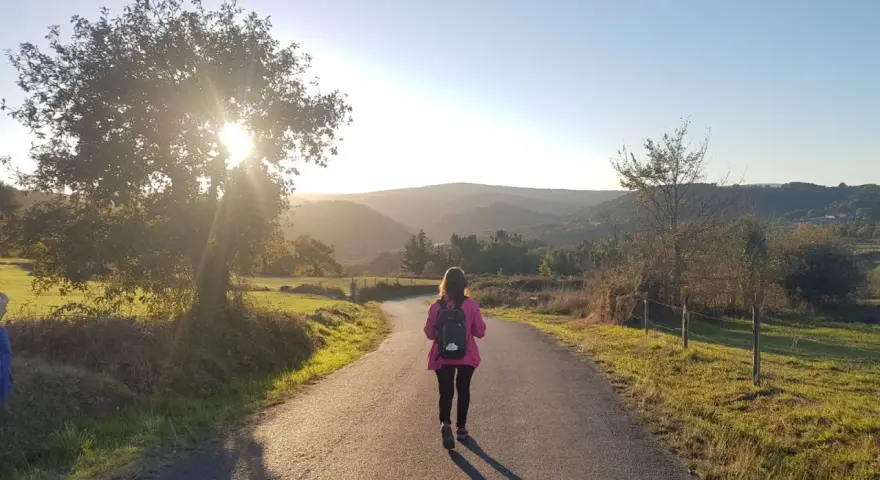 Una peregrina con mochila rosa camina por un sendero rural al atardecer, disfrutando del **camino de Santiago corriendo**.